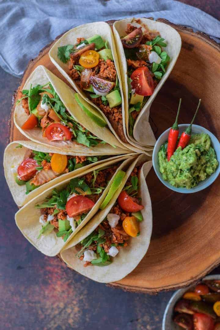 Refried Bean Tacos spread perfectly around wooden cutting board with guacamole.