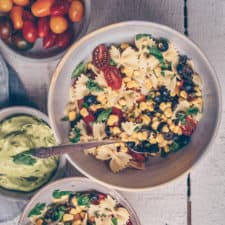 Bowl of bow tie pasta salad surrounded by fresh vegetable ingredients