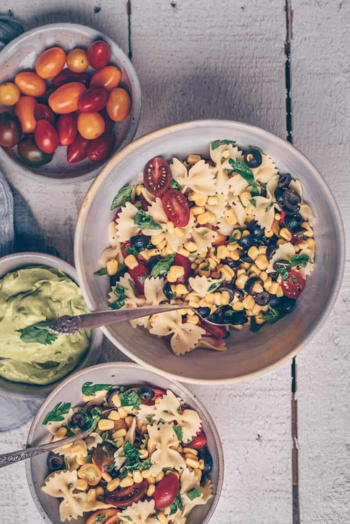 Bowl of bow tie pasta salad surrounded by fresh vegetable ingredients