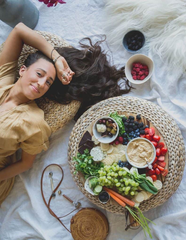 Maria laying down next to a vegetable spread on a cutting board with lentil hummus.