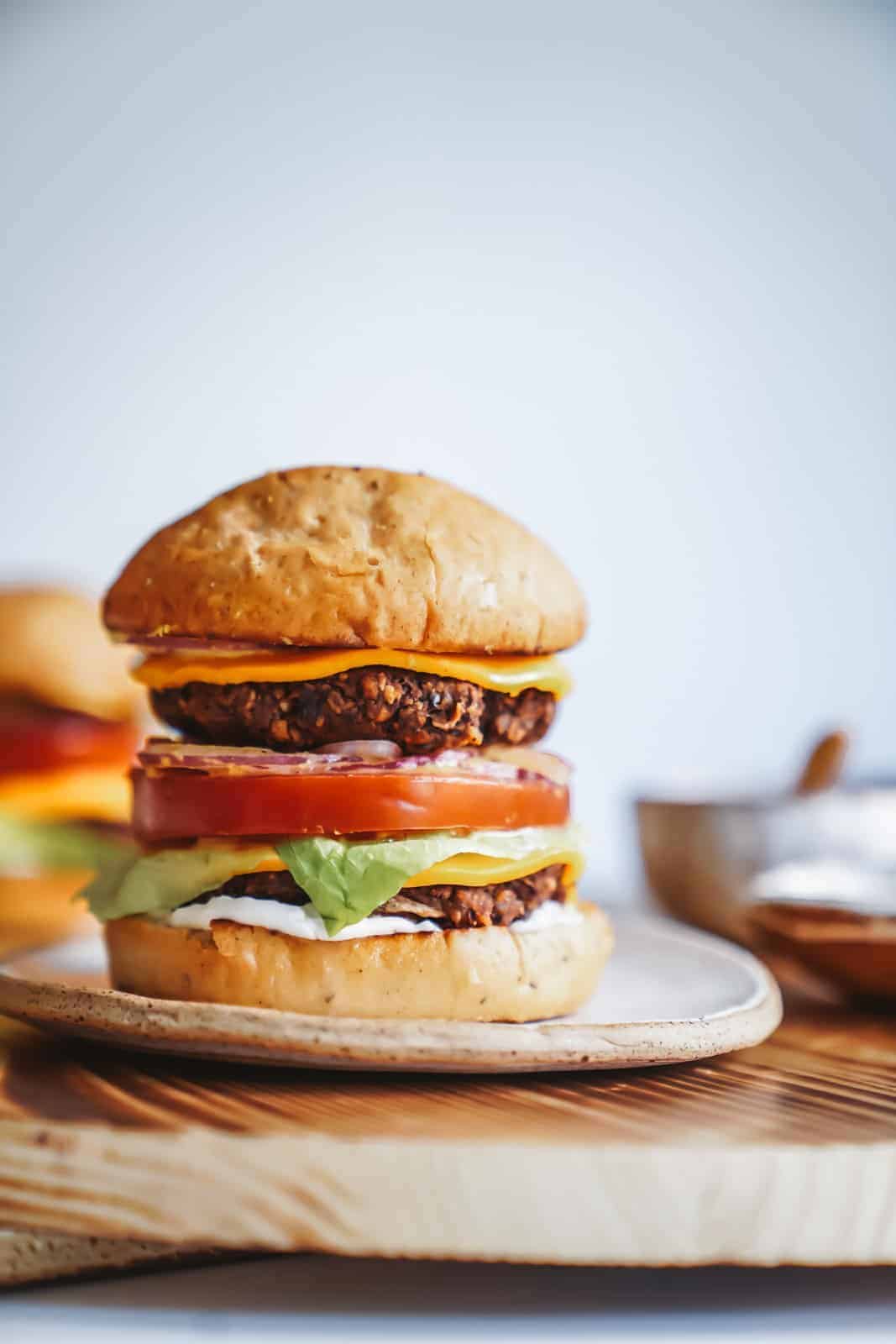 An unreal layered vegan burger stacked with all the fixings sitting on a serving dish.