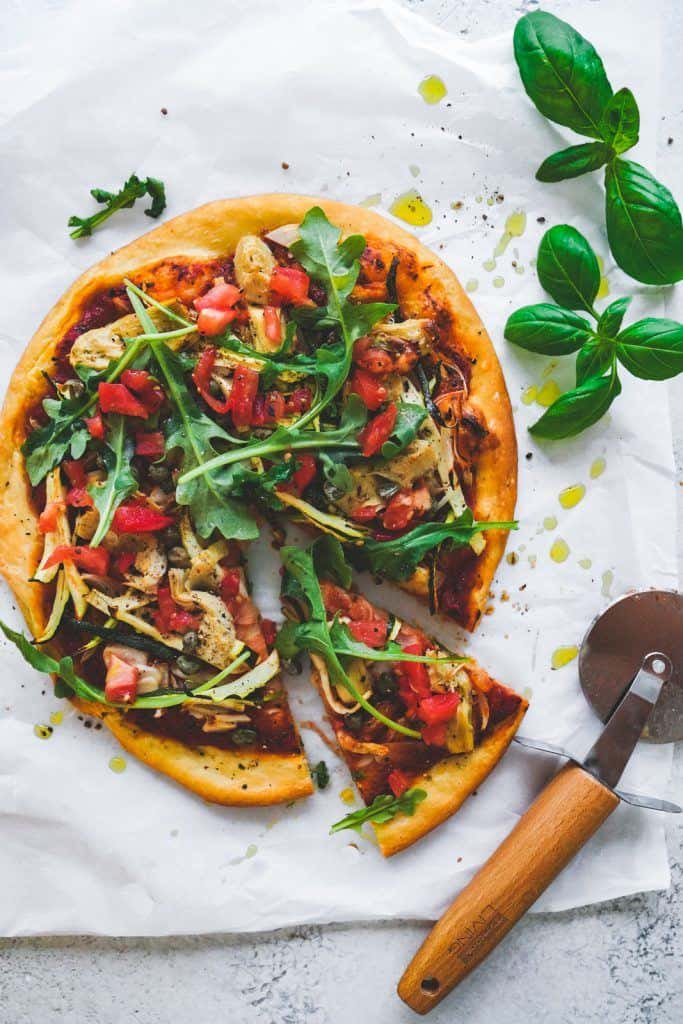 Plant-based pizza on a platter with a pizza cutter