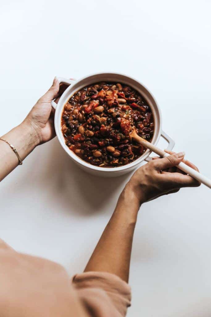 Serving bowl of lentil chili with hand stirring the pot.