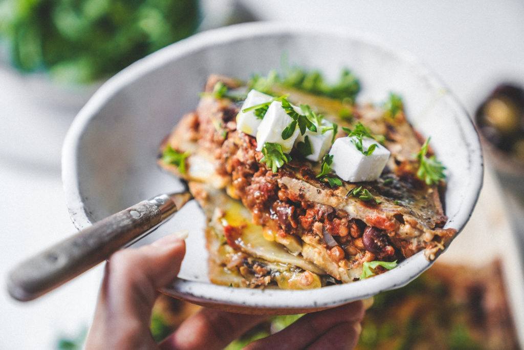 Big bowl of vegan moussaka ready to be eaten with fresh vegan feta and herbs.