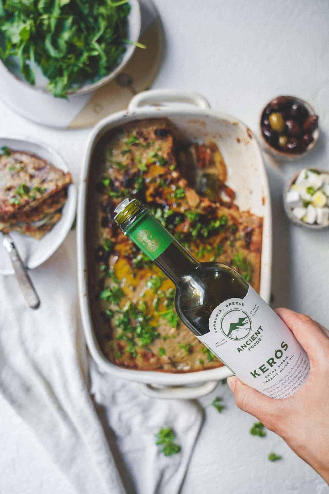 Olive oil being poured onto the cooked vegan moussaka. 