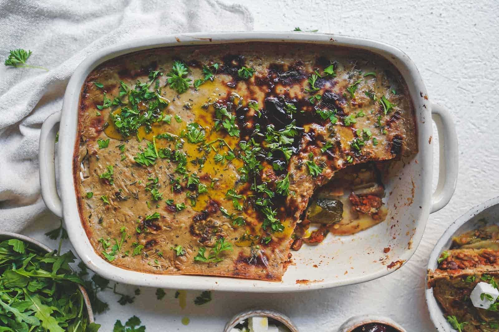 A big casserole dish filled with Vegan Moussaka ready to be eaten and sprinkled with fresh herbs.