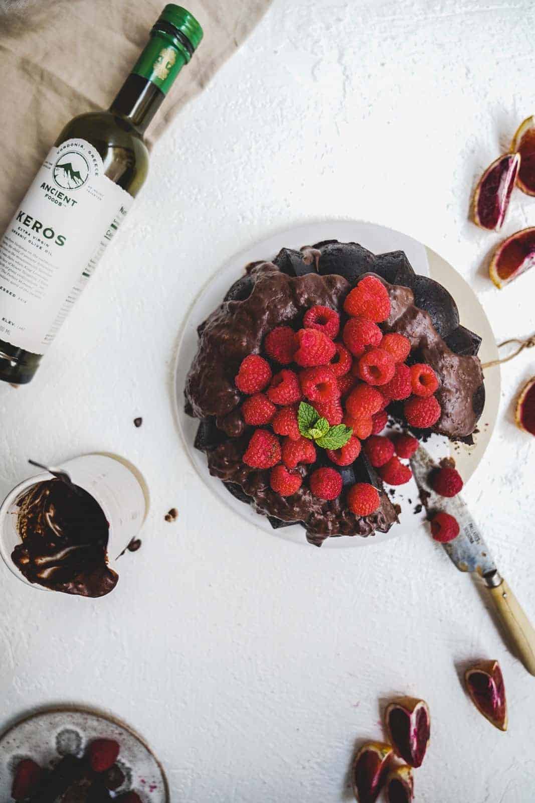 Delicious bundt cake sitting on white table with beautiful red fresh raspberries to decorate the top.