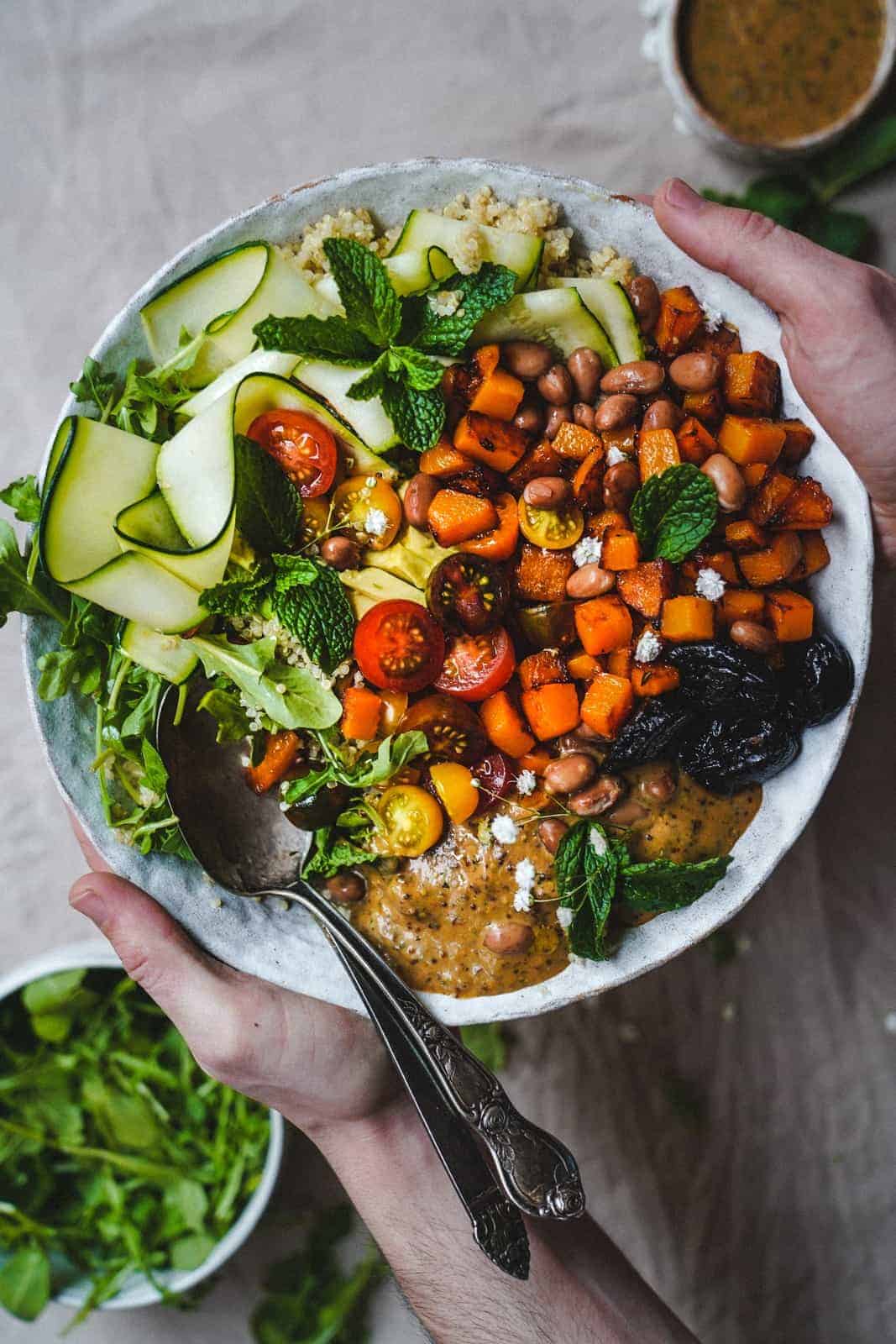 A set of hands holding a big bowl loaded with vegetables with a serving spoon.