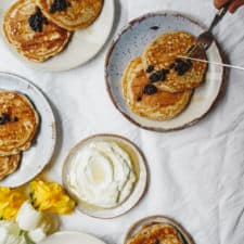 Plates of pancakes scattered on white table with yummy berry simple syrup on top.