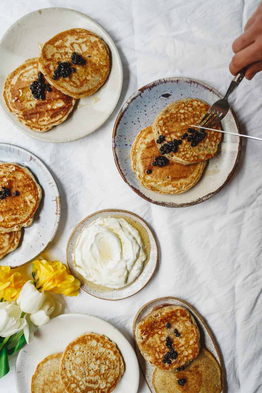 Plates of pancakes scattered on white table with yummy berry simple syrup on top.