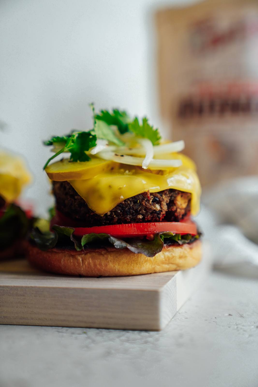 A black bean vegan burger sitting on the ledge of a cutting board with all the fixings.