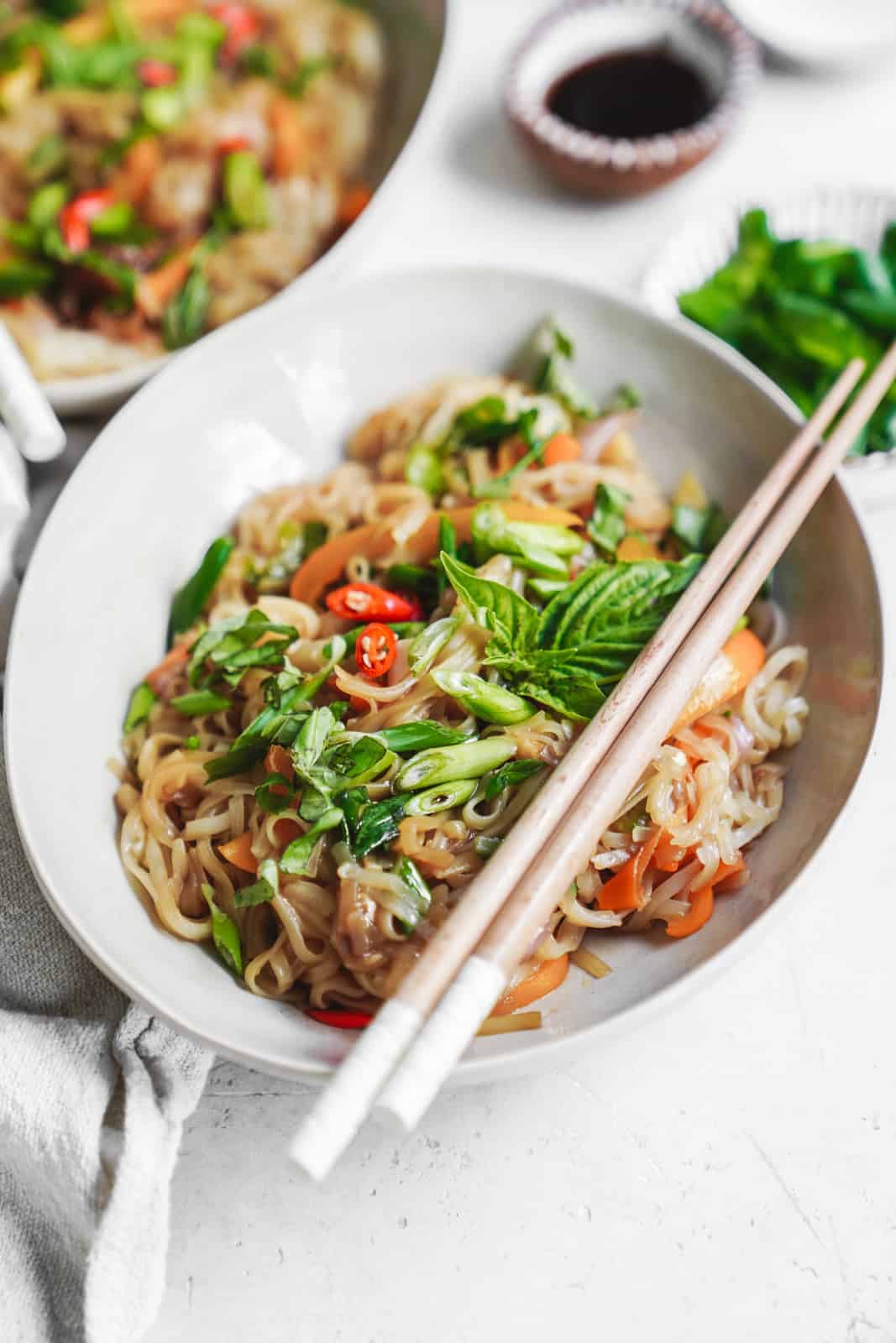 White bowl of drunken noodles with chopsticks. Topped with fresh herbs.