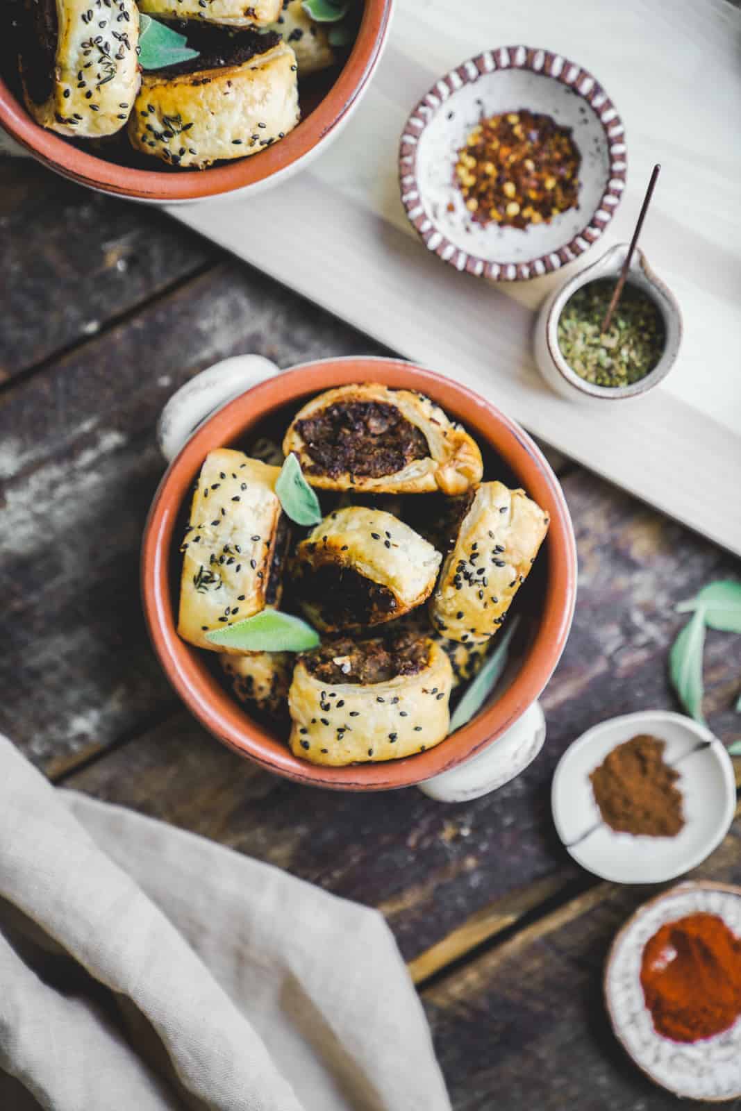 Bowl of vegan sausage rolls surrounded by spices. 