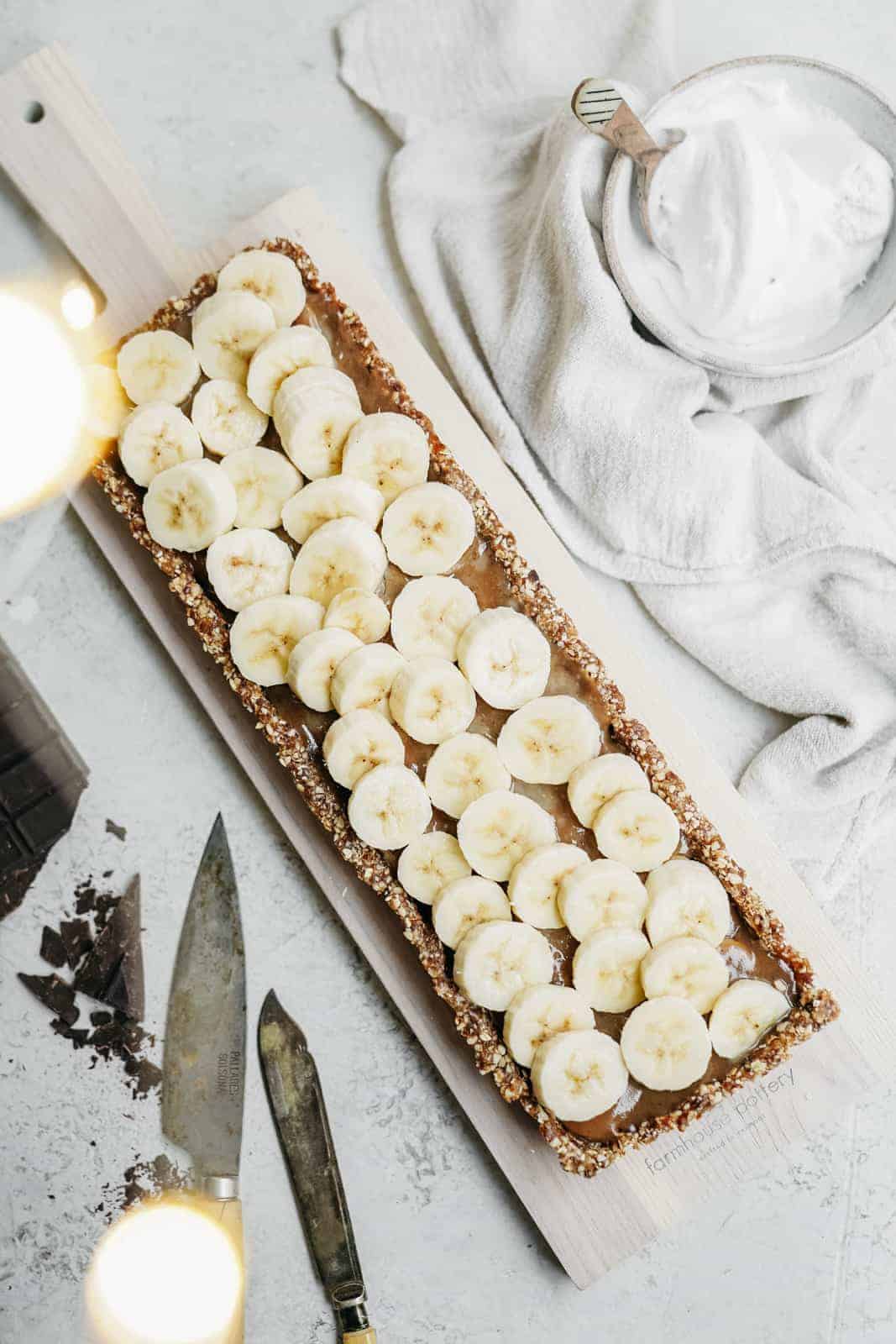 vegan banoffee pie on countertop with fresh bananas on top.