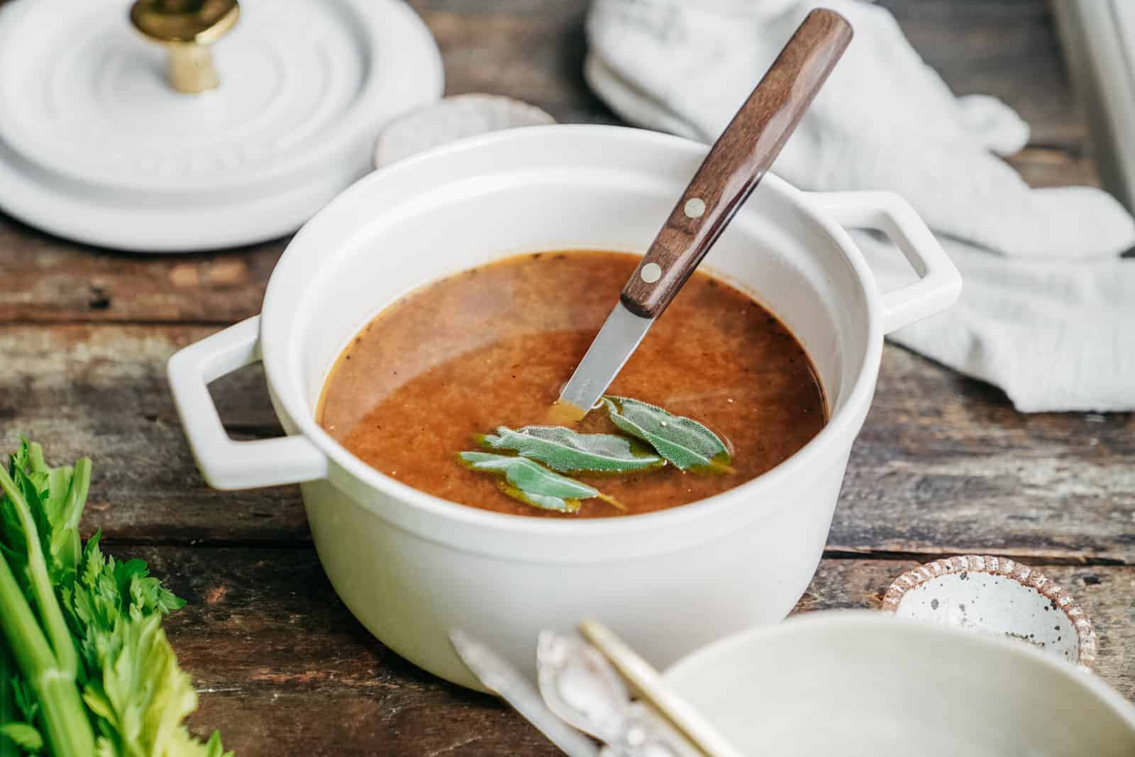 Small serving bowl of homemade vegetable stock with fresh herbs on top.