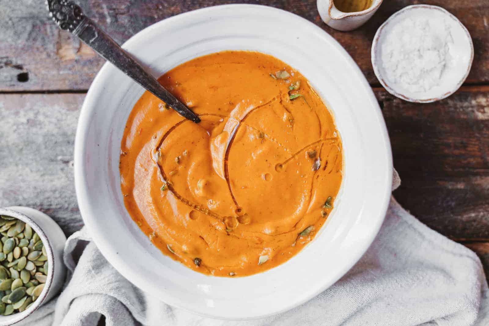 A big bowl of bright orange carrot soup with a drizzle of olive oil. Vegan, and dairy-free.