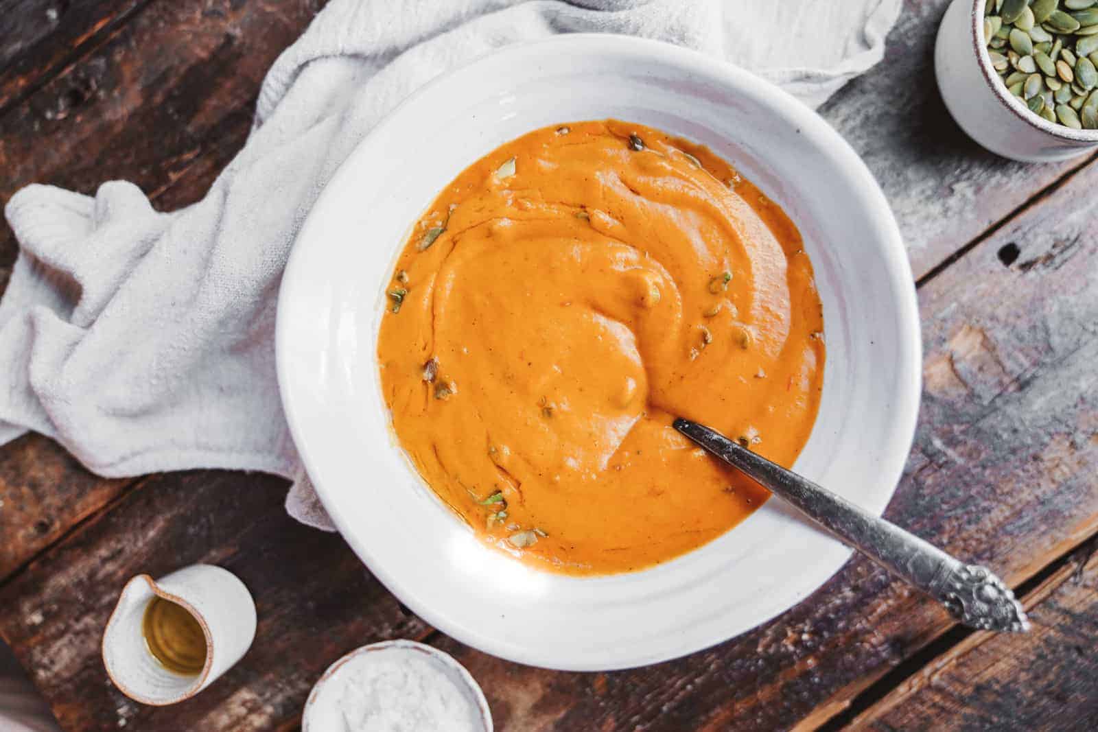 A spoon in a big bowl of creamy vegan carrot soup ready to be devoured at the table.