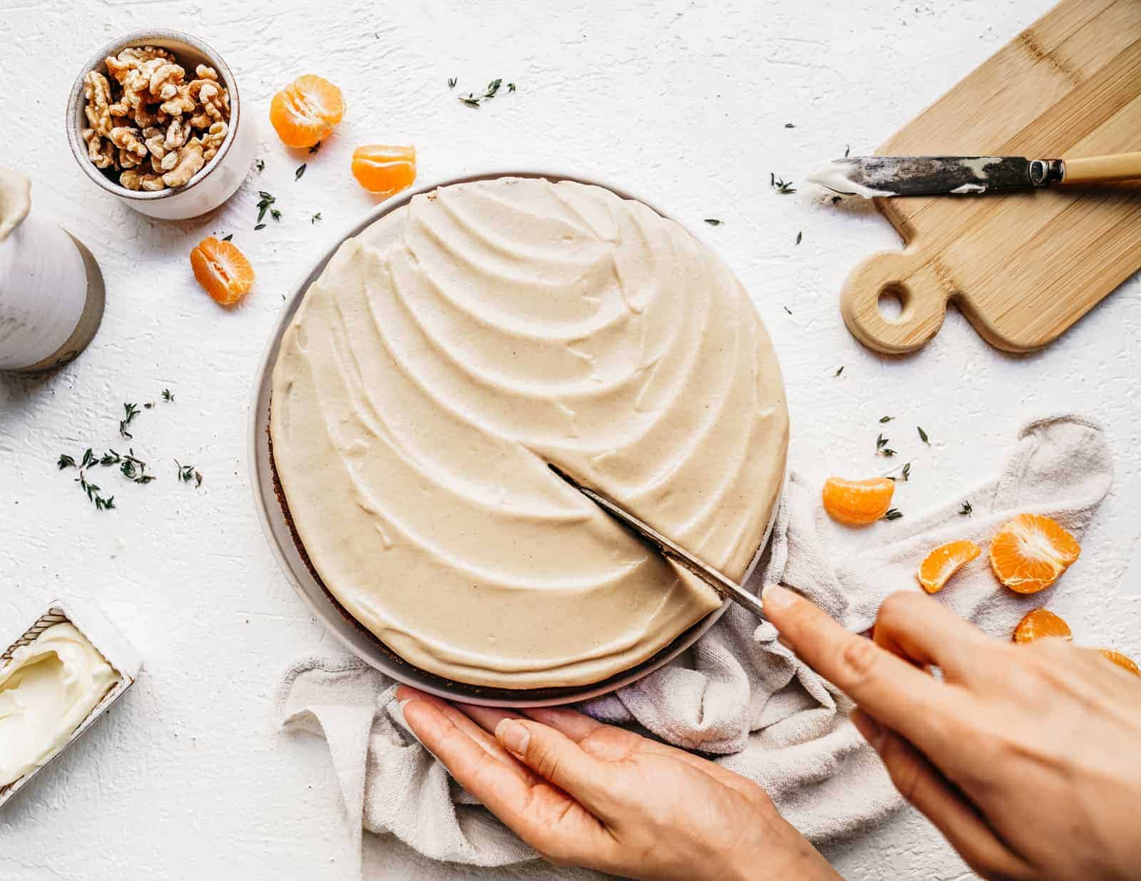 Vegan carrot cake on counter with knife cutting into it ready to be eaten.