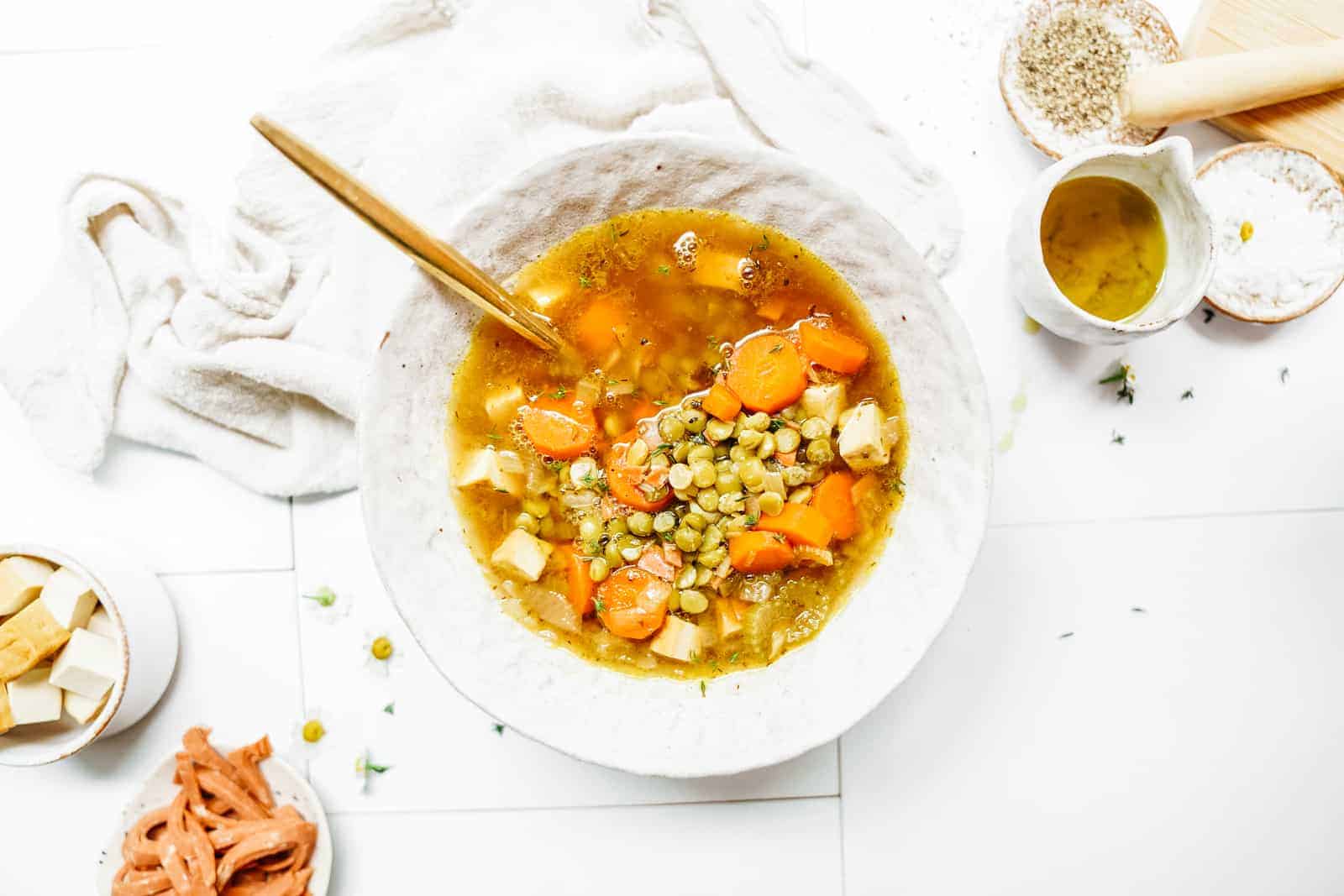 Vegan Split Pea Soup sitting in white bowl on countertop surrounded by ingredients.