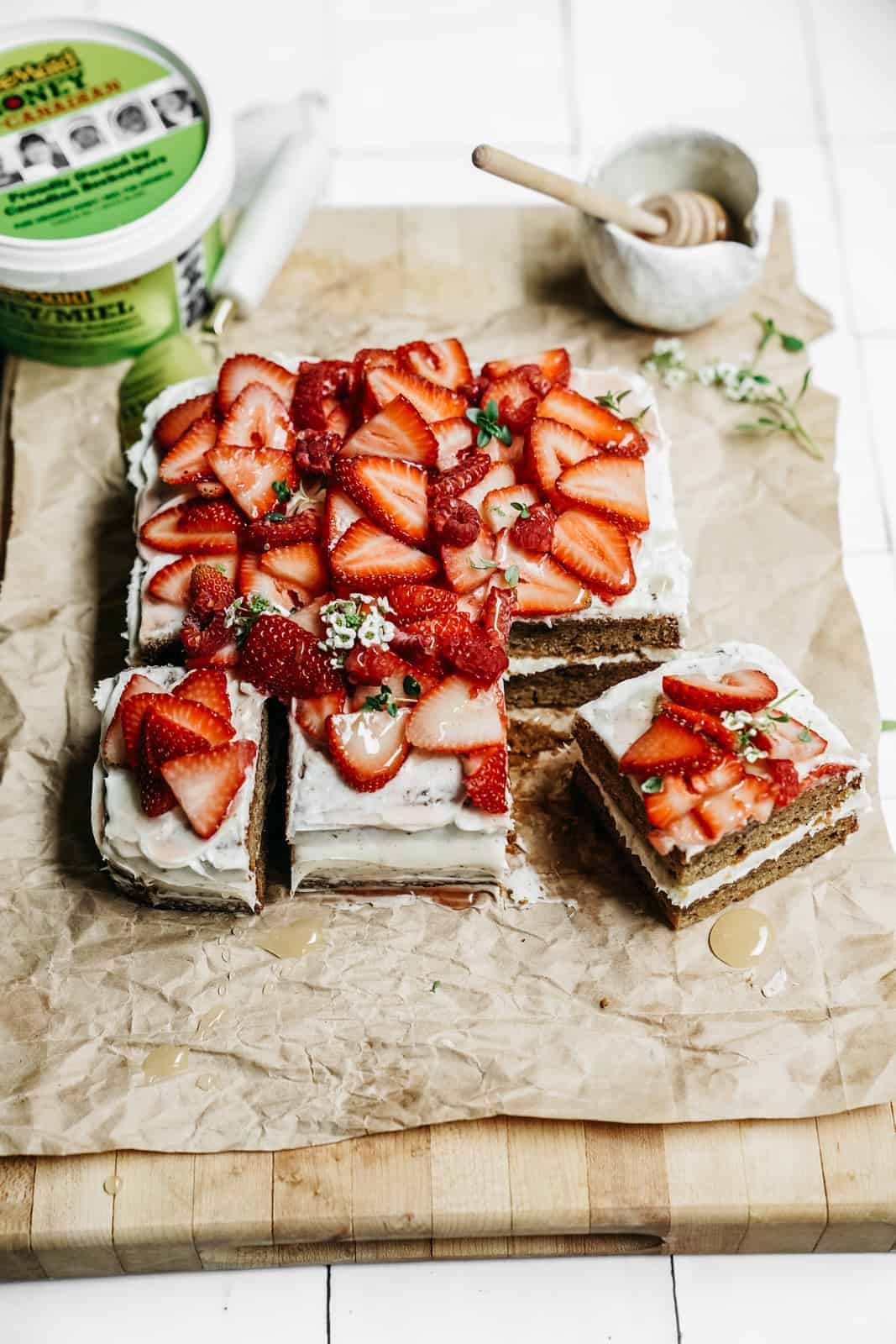 Bee Maid Honey sitting on cutting board with beautiful sliced Honey Cake topped with strawberries.