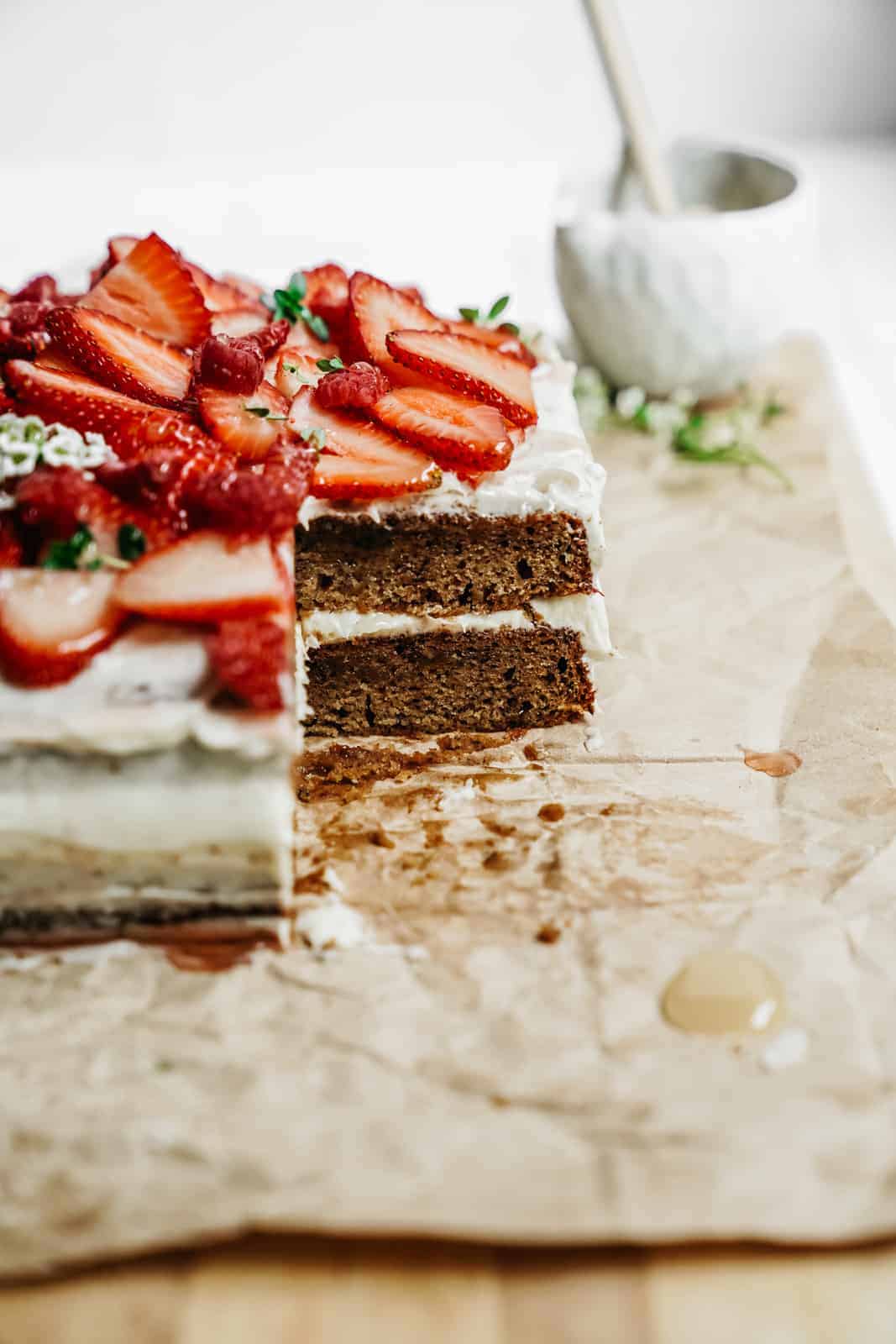 Easy Honey Cake with a slice out of it and topped with lush red strawberries.