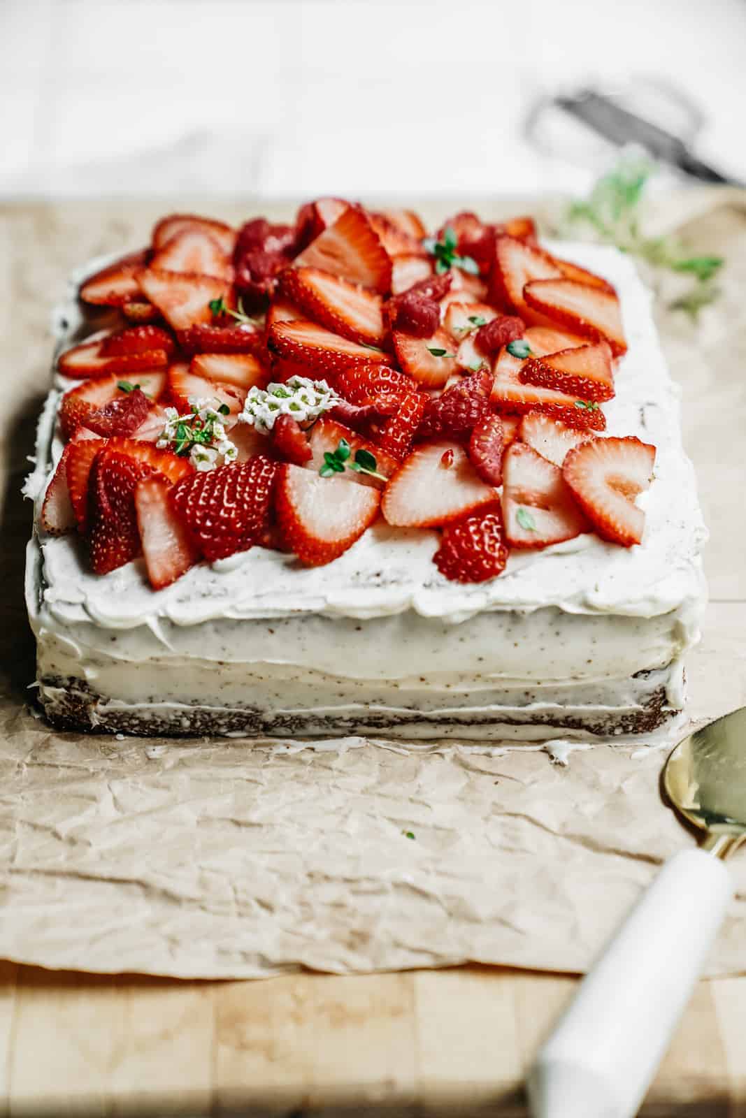 Yummy spring Vanilla Honey Cake sitting on a cutting board with fresh strawberries sliced on top.