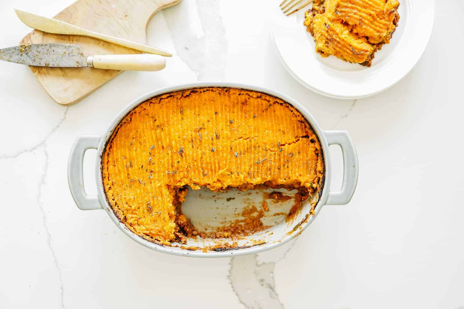 A casserole dish filled with Shepherd's Pie with a slice taken out of it.