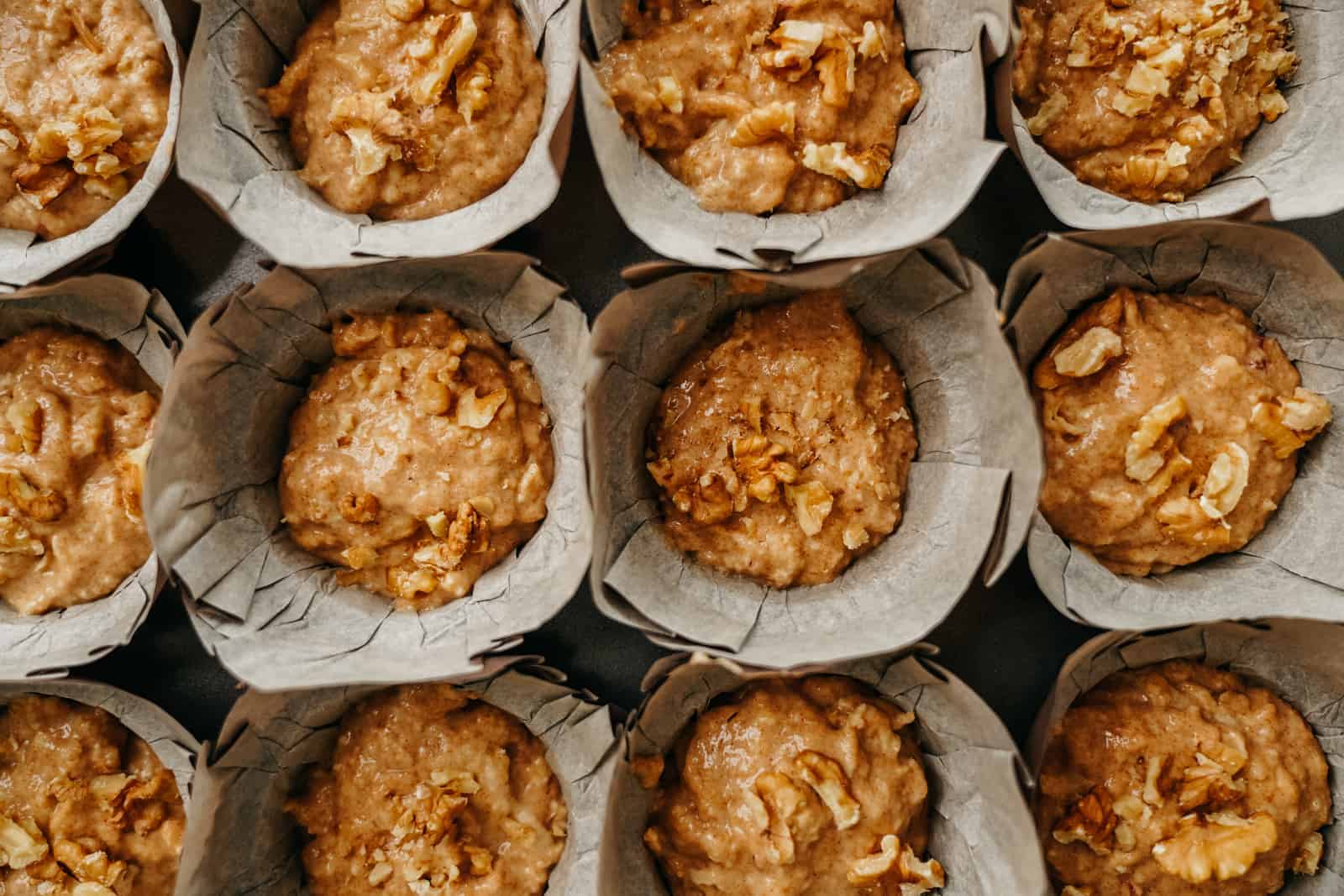 A dozen Vegan Apple Cinnamon Muffins all lined up in muffin wrappers on counter.