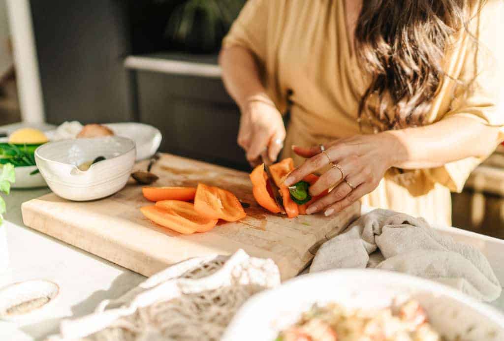 Maria cutting a orange bell pepper on cutting board to show her interacting with food. A food photograph tip.