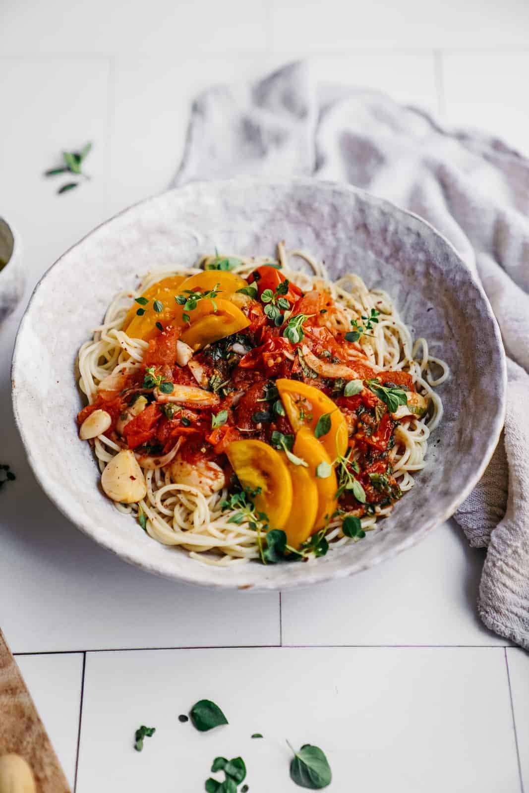 Big white bowl of Vegan Tomato and Garlic Pasta on a counter surrounded by little bowls of fresh ingredients.