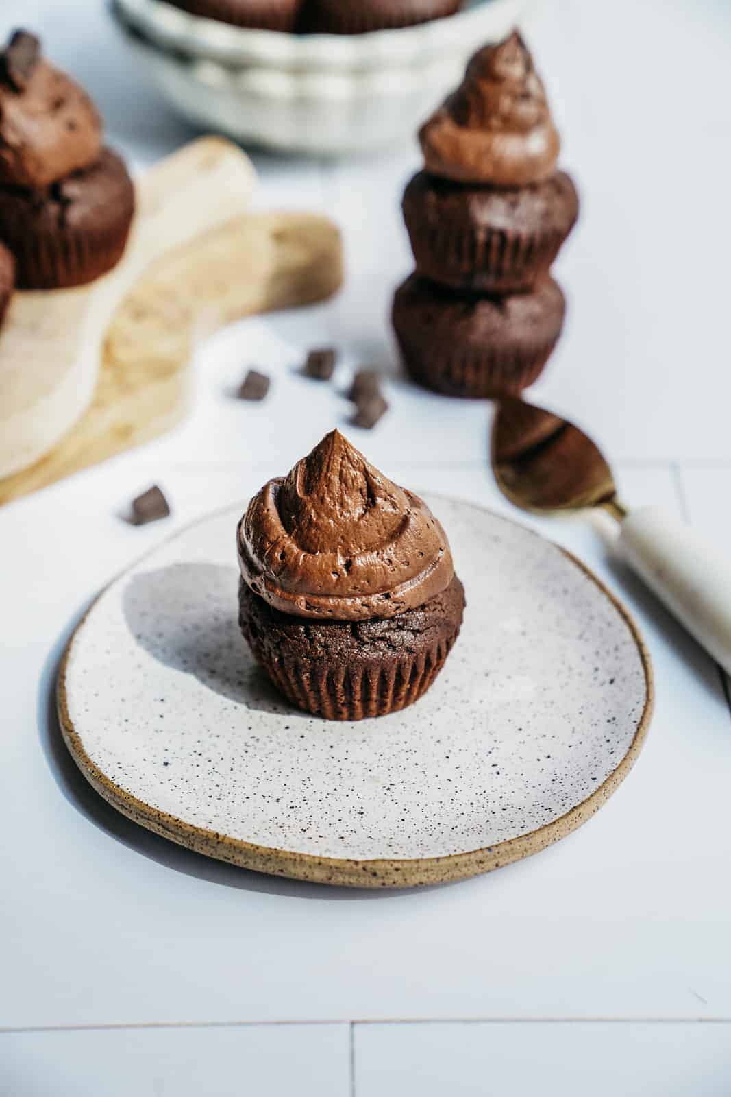 A brownie chocolate muffin sitting on a plate with a dollop of cashew chocolate icing.