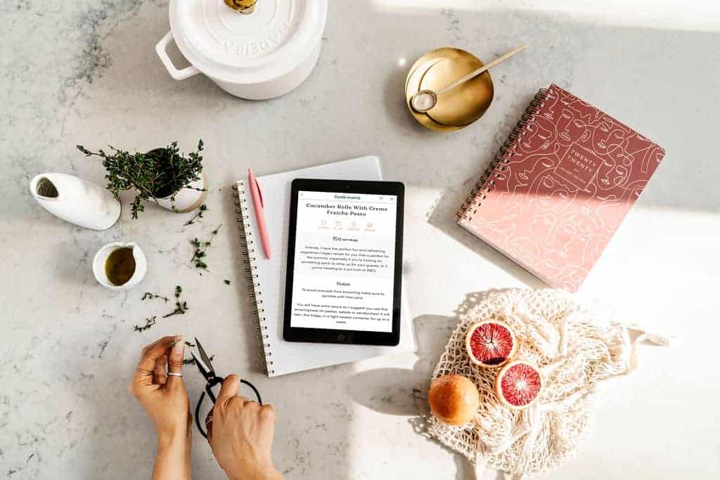 A food bloggers workspace with notebooks, an iPad and photography food supplies scattered on table.