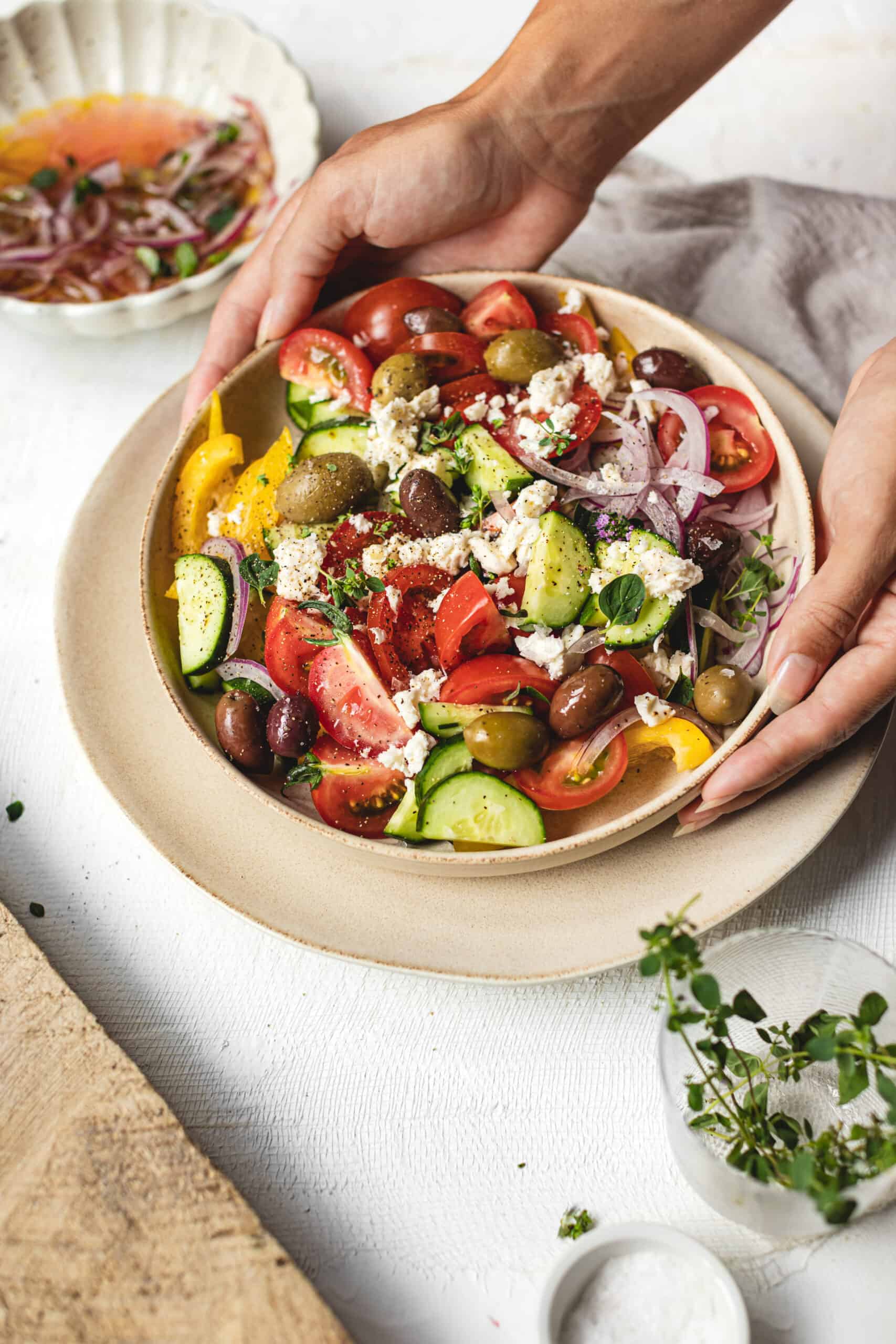 Big colorful bowl of Greek Salad Recipe with hands placing it on table