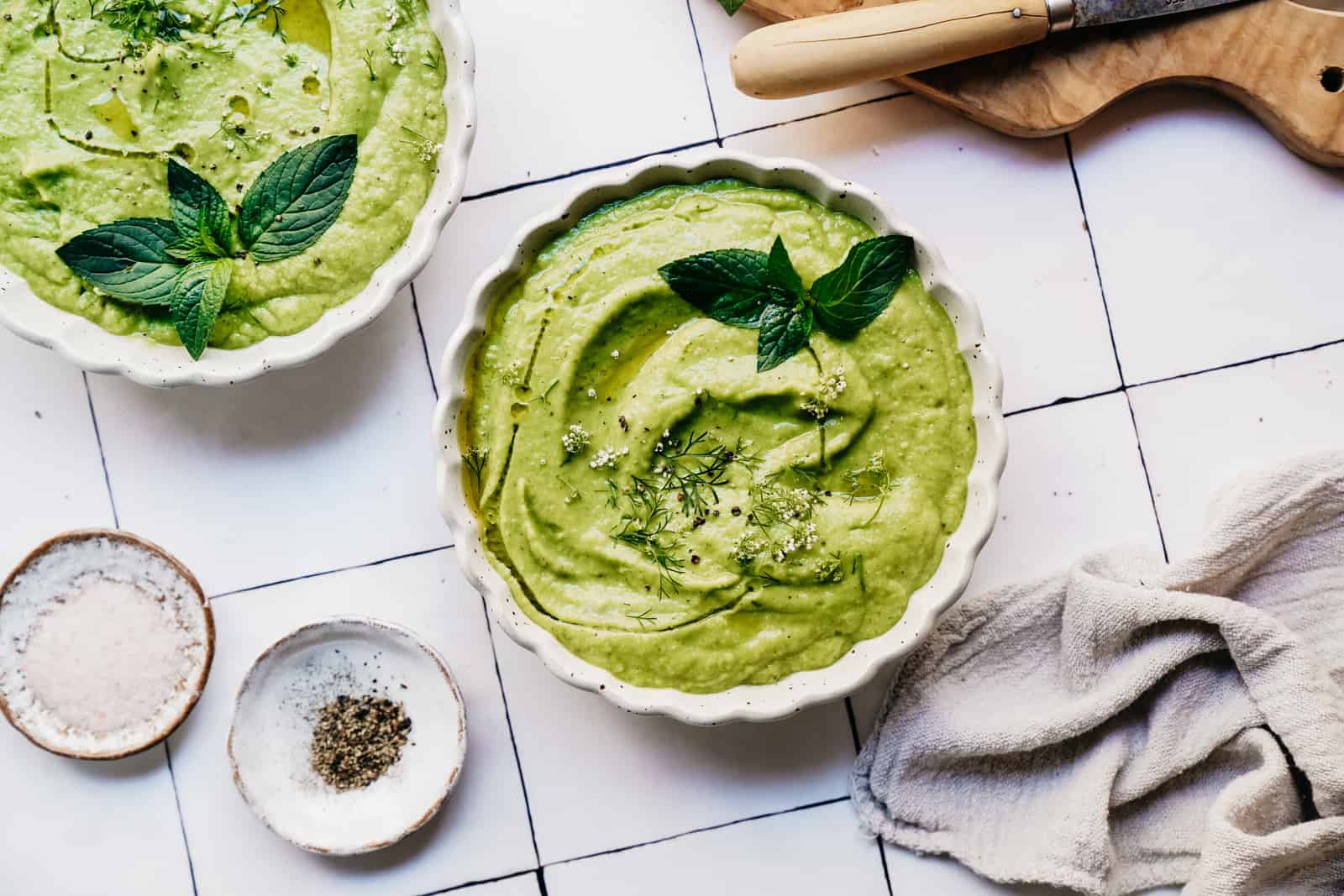 Bowls of creamy zucchini gazpacho topped with mint on countertop.