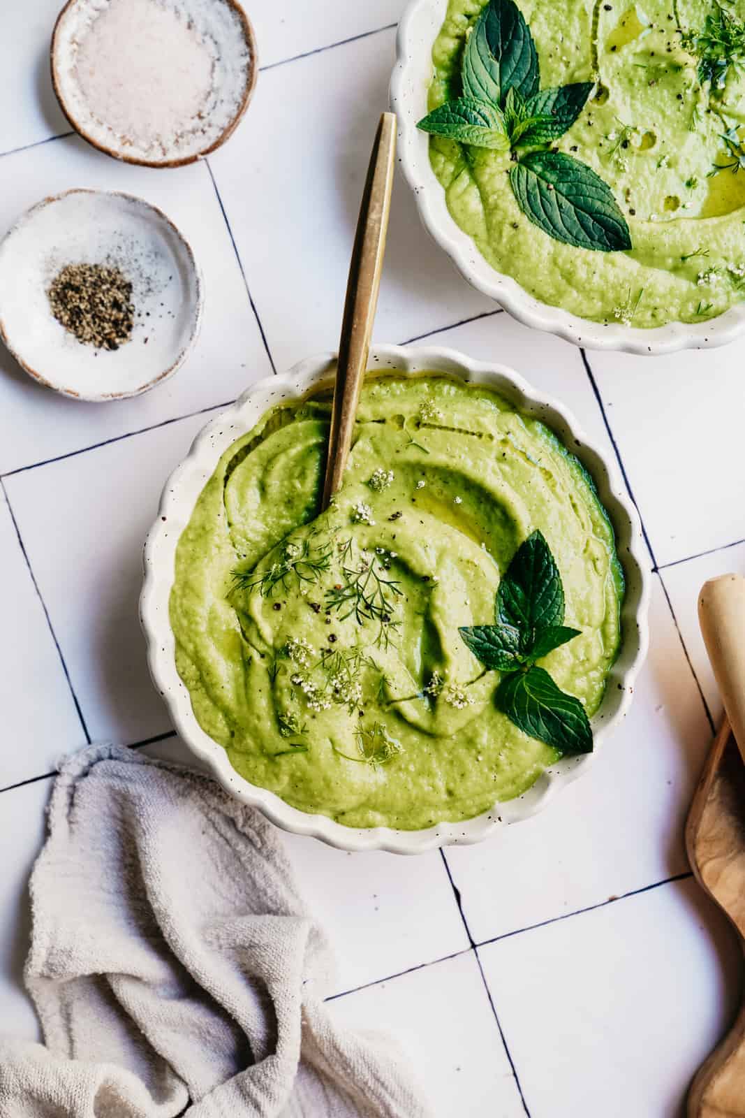 Big bowl of creamy Vegan Zucchini Gazpacho in a white bowl on a white countertop.