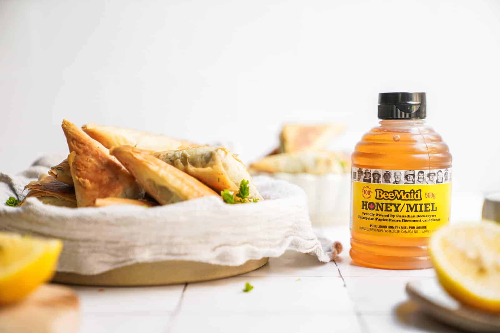 Bottle of honey on countertop surrounded by ingredients and mushroom pastry bites.