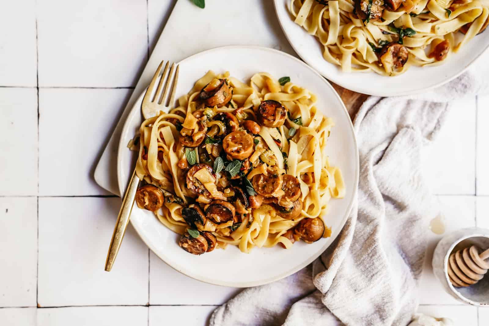 Plate of Vegan Sausage Pasta with gold fork on countertop.