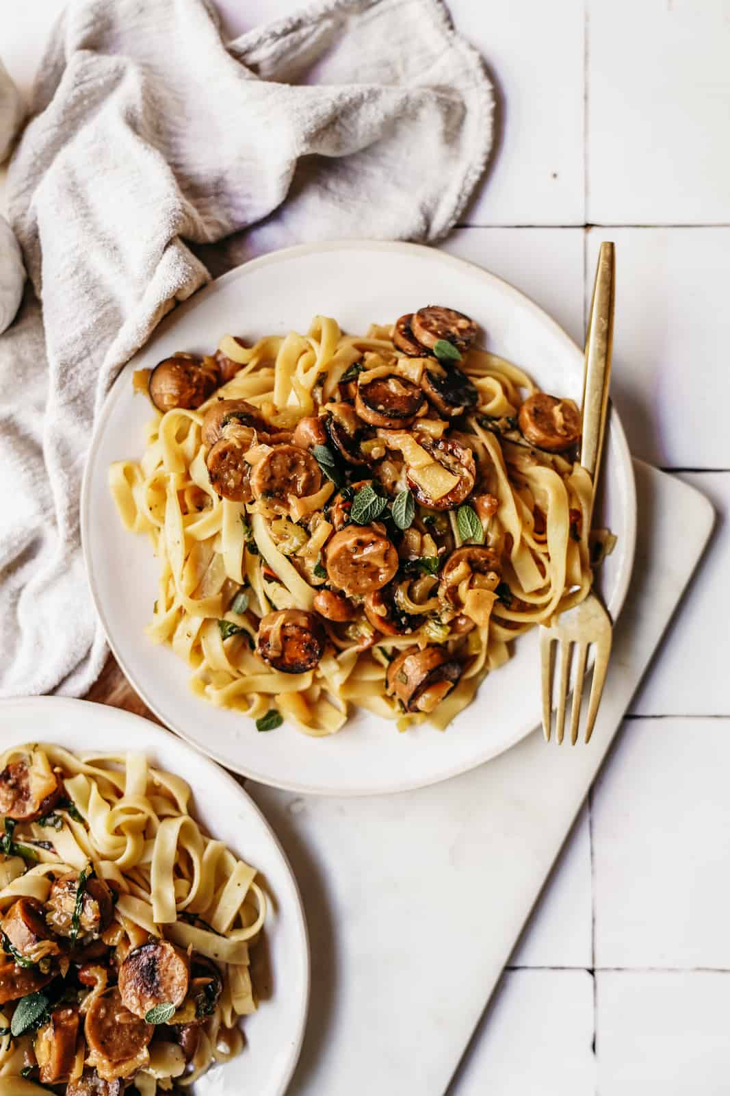 White plate of vegan sausage pasta on countertop with fork.