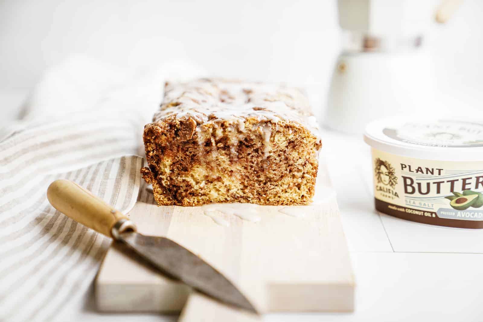 Vegan Cinnamon Bun Bread sliced on cutting board next to Califia Farms Plant Butter