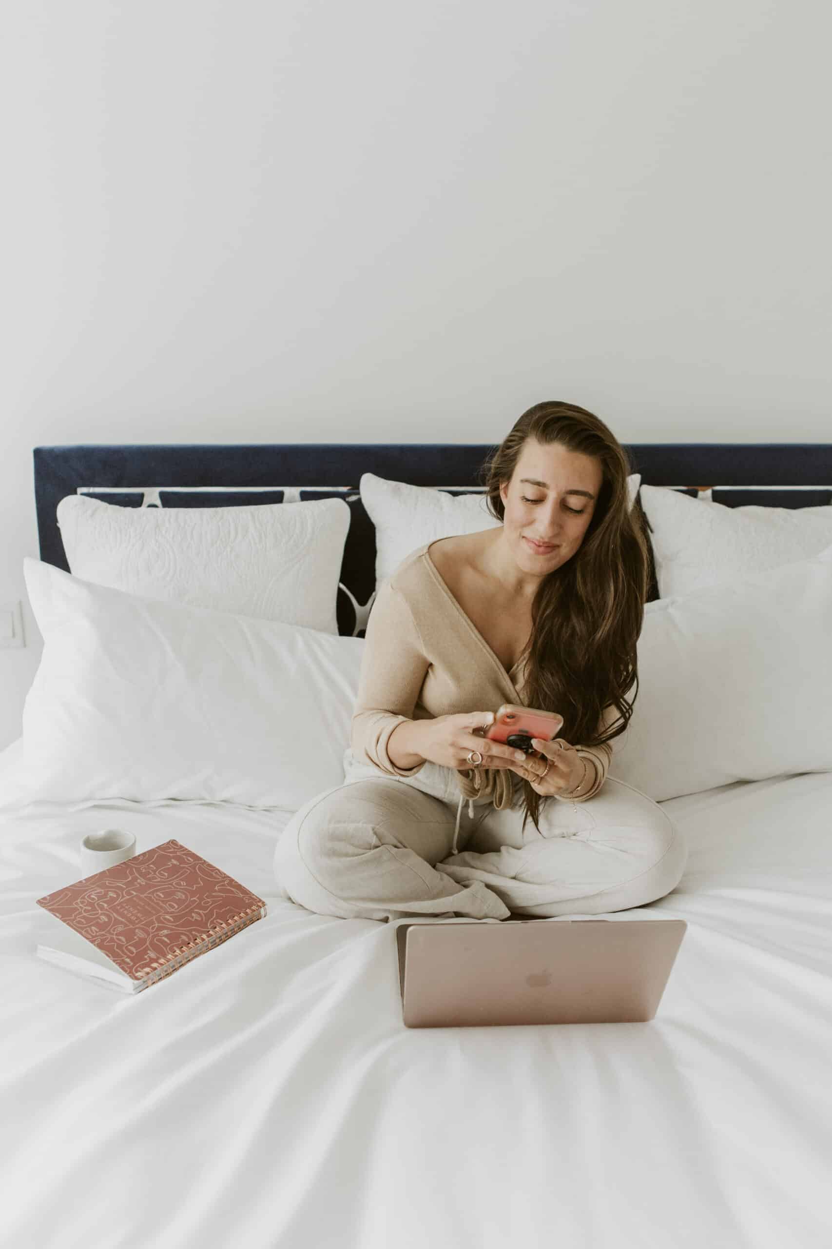 Food blogger, Maria, sitting on her bed on her phone and working at her computer.