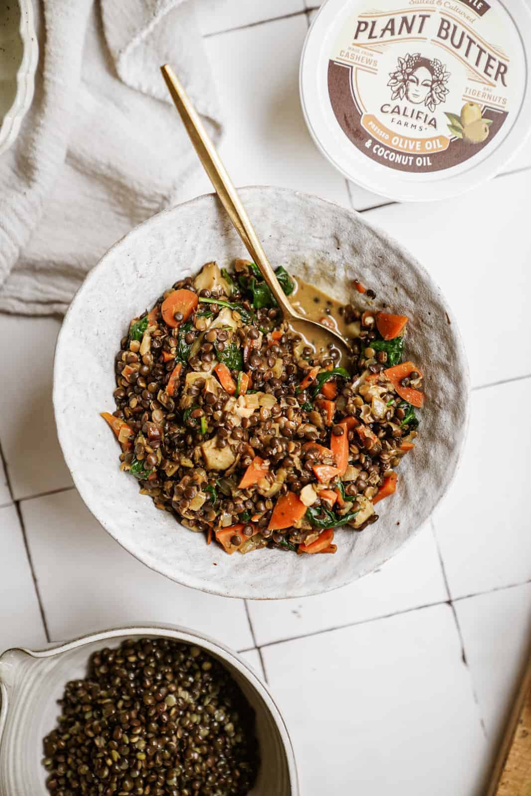 Lentils with Spinach in serving dish with spoon in the bowl next to Califia Farms Plant Butter