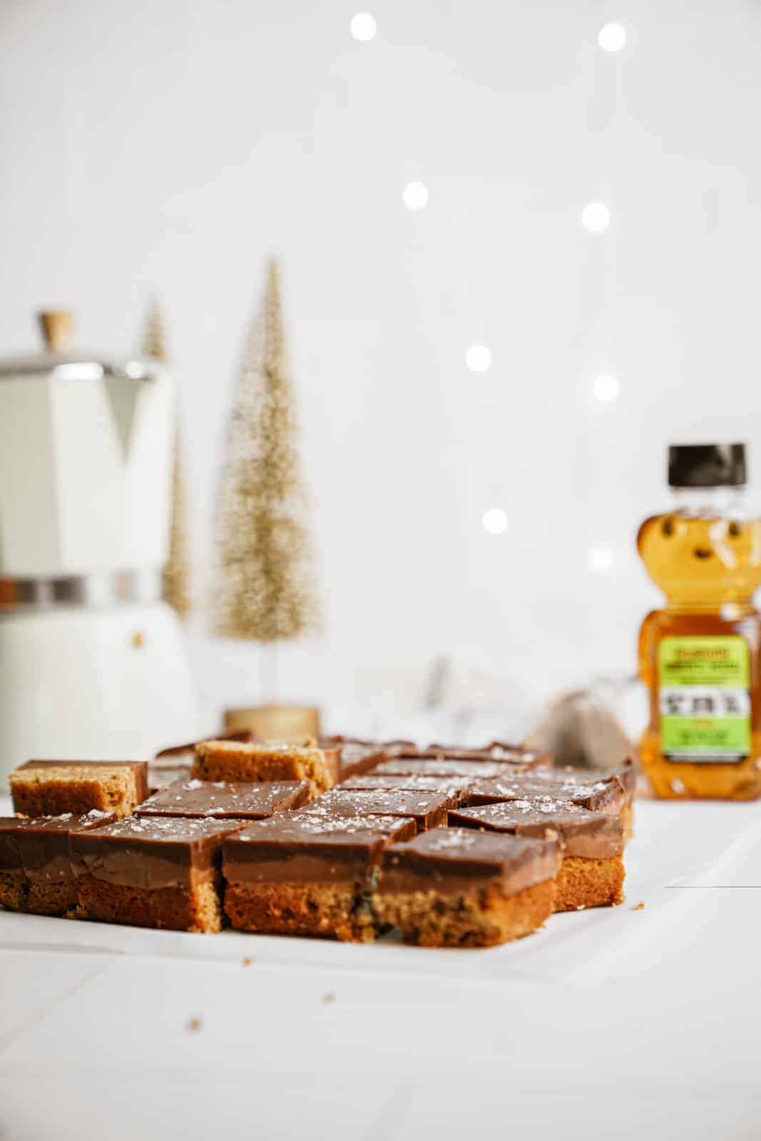 Caramel pretzel bars on a countertop with holiday backdrop, next to a BeeMaid honey container.