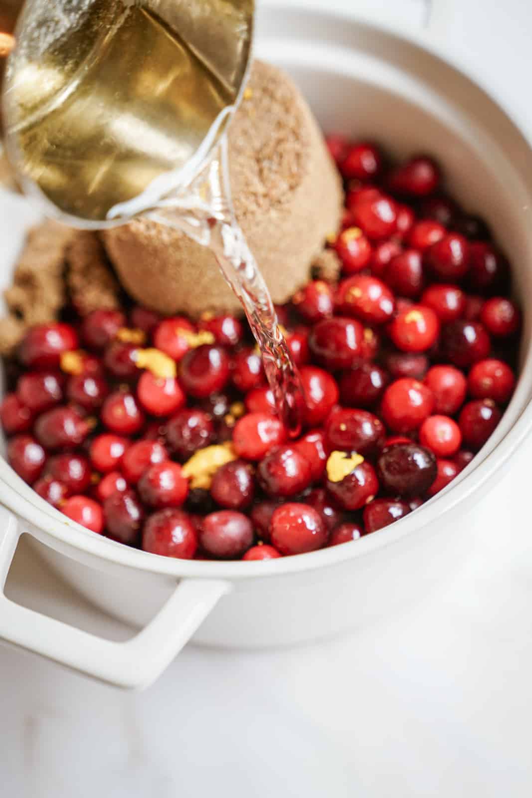 Water being added to fresh cranberries and sugar for vegan cranberry sauce