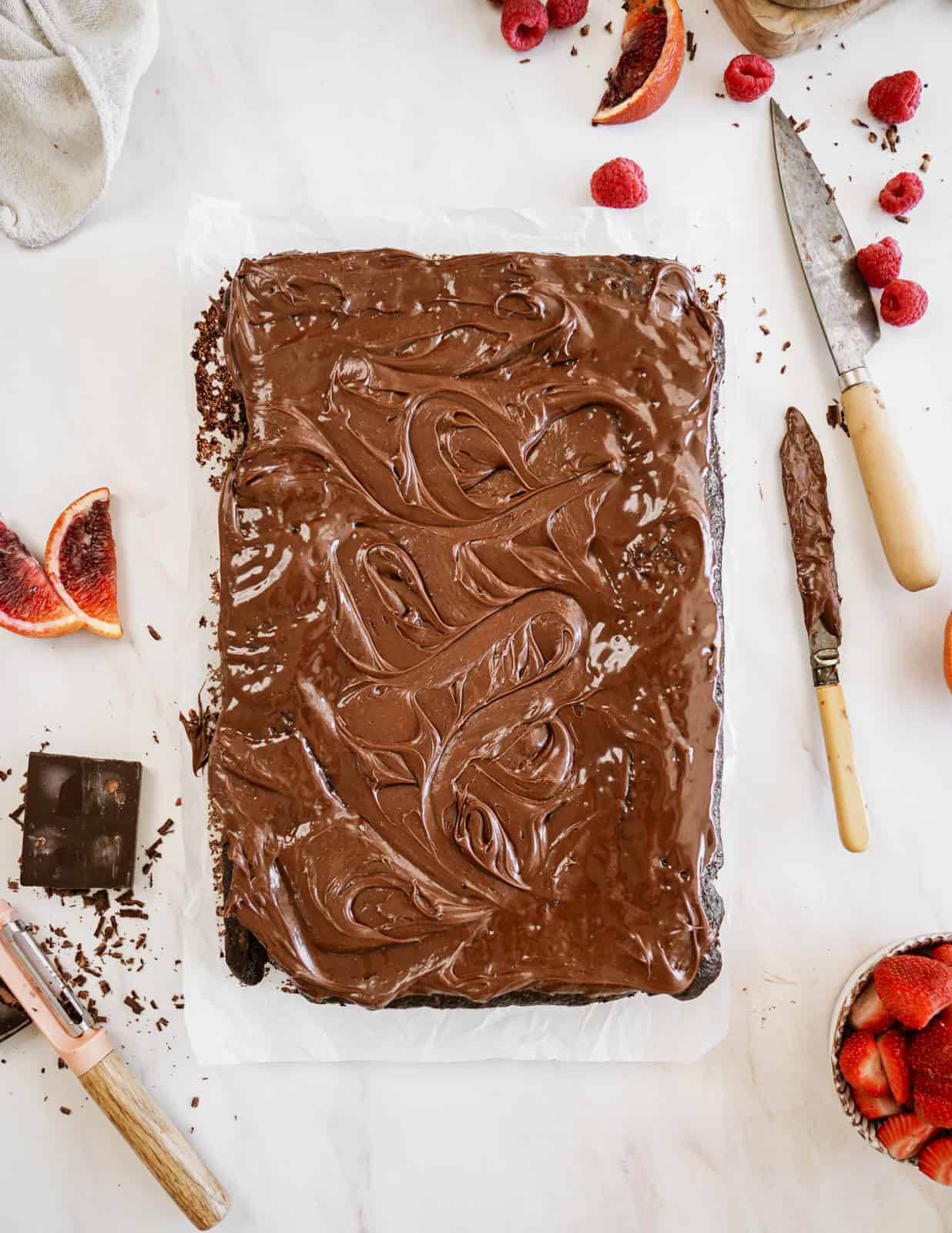 Overhead view of vegan sheet cake on countertop surrounded by berries and ingredients.