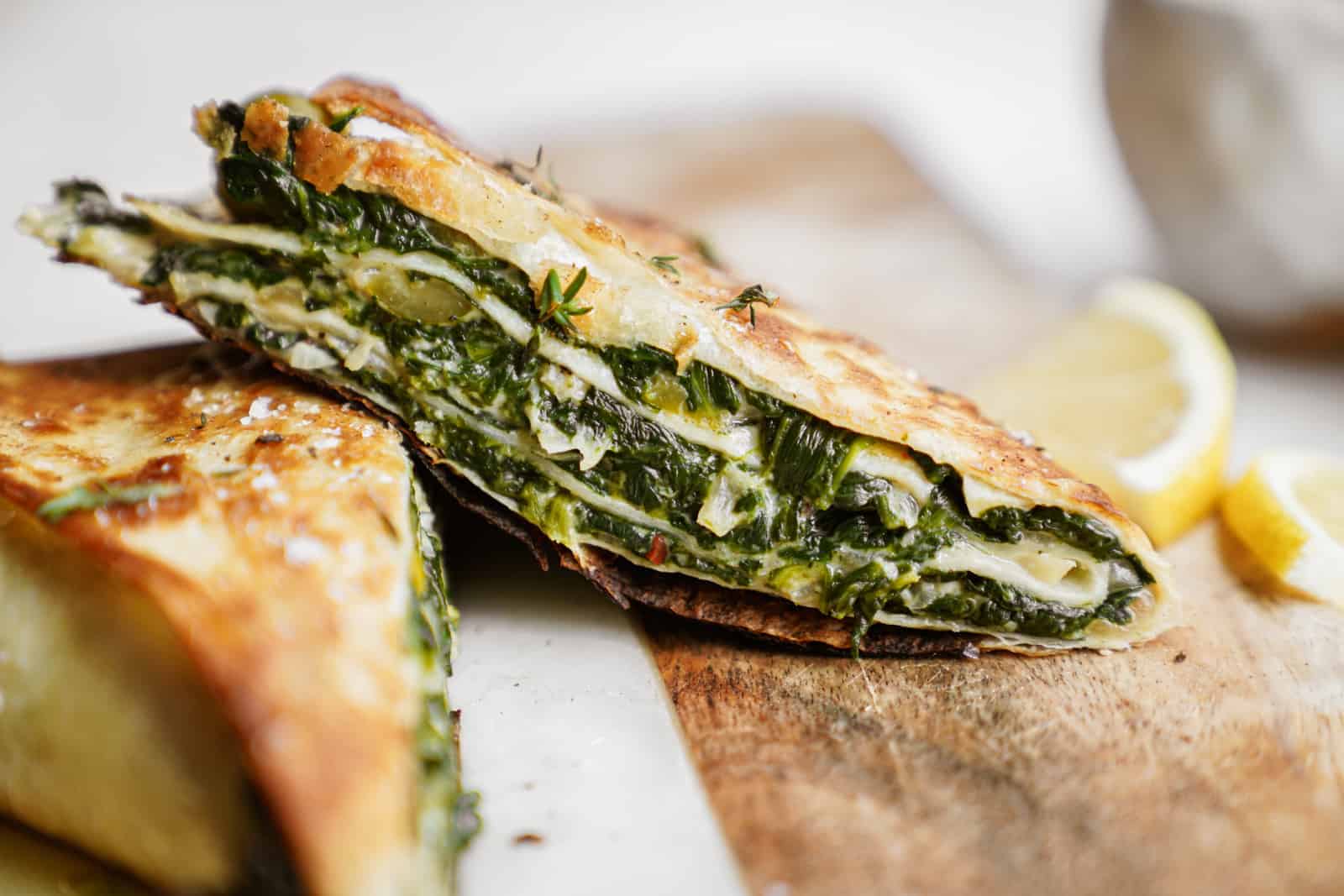 Trendy spinach wrap made greek-style cut into triangles on countertop.