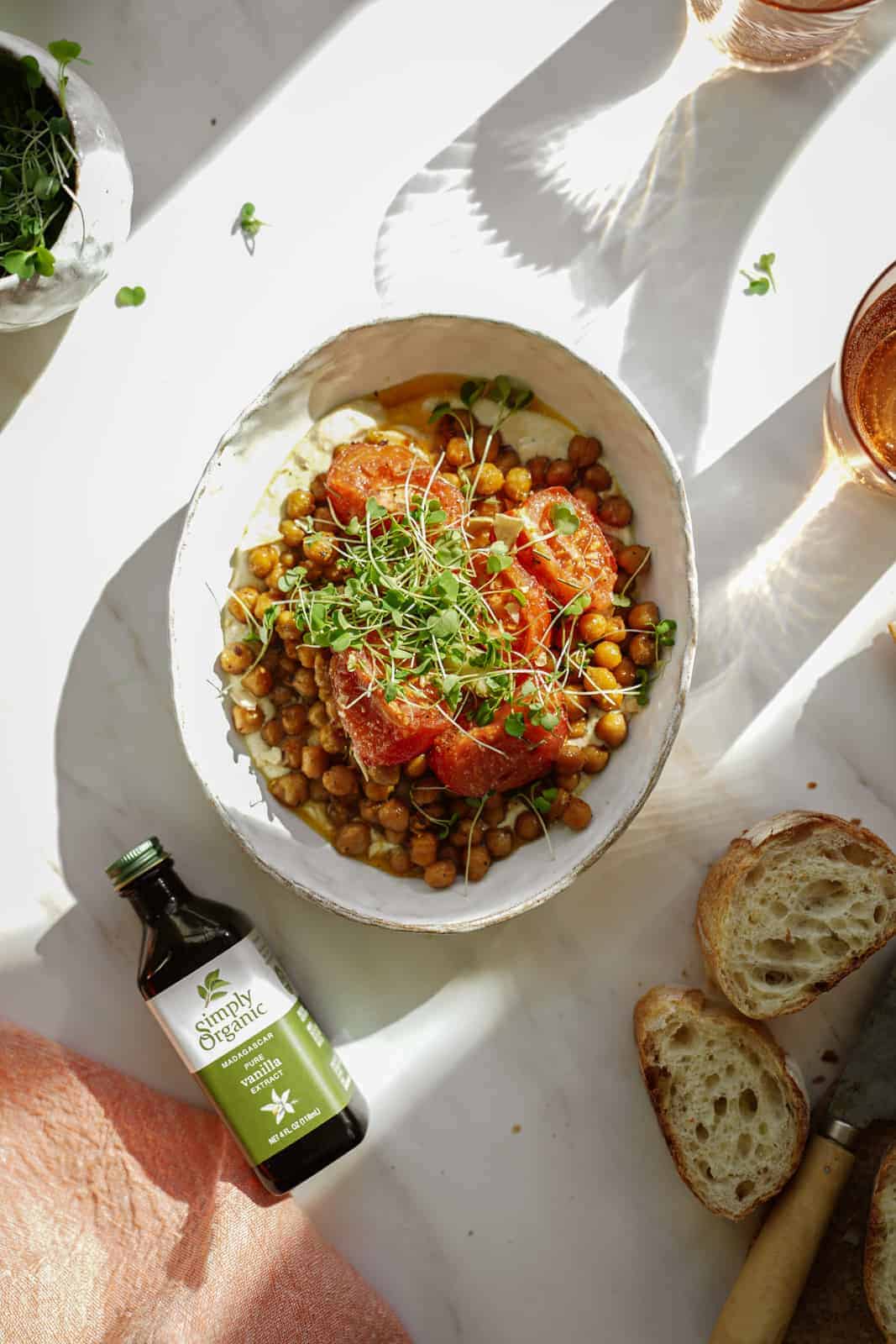 oven-roasted chickpeas in a white bowl with slices of bread next to it and a bottle of vanilla