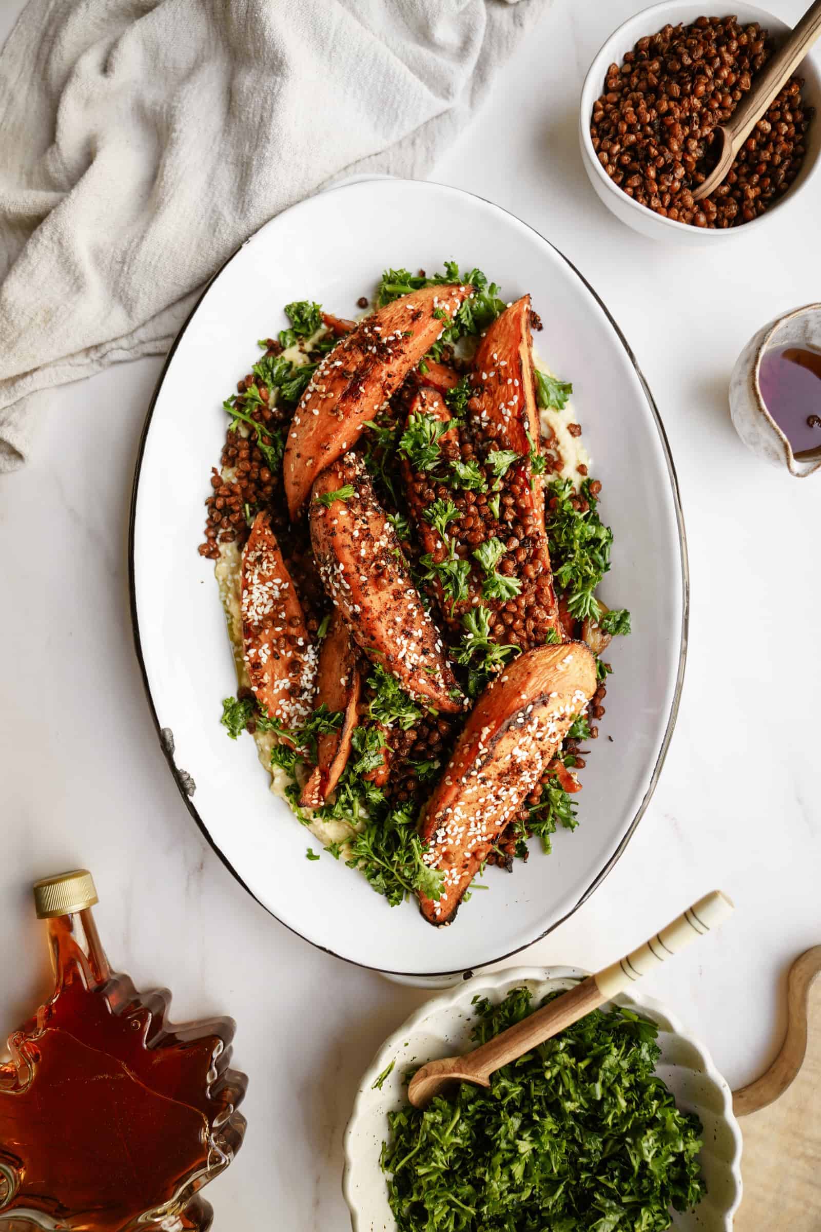 Roasted sweet potatoes on a dish with fresh herbs, surrounded by ingredients