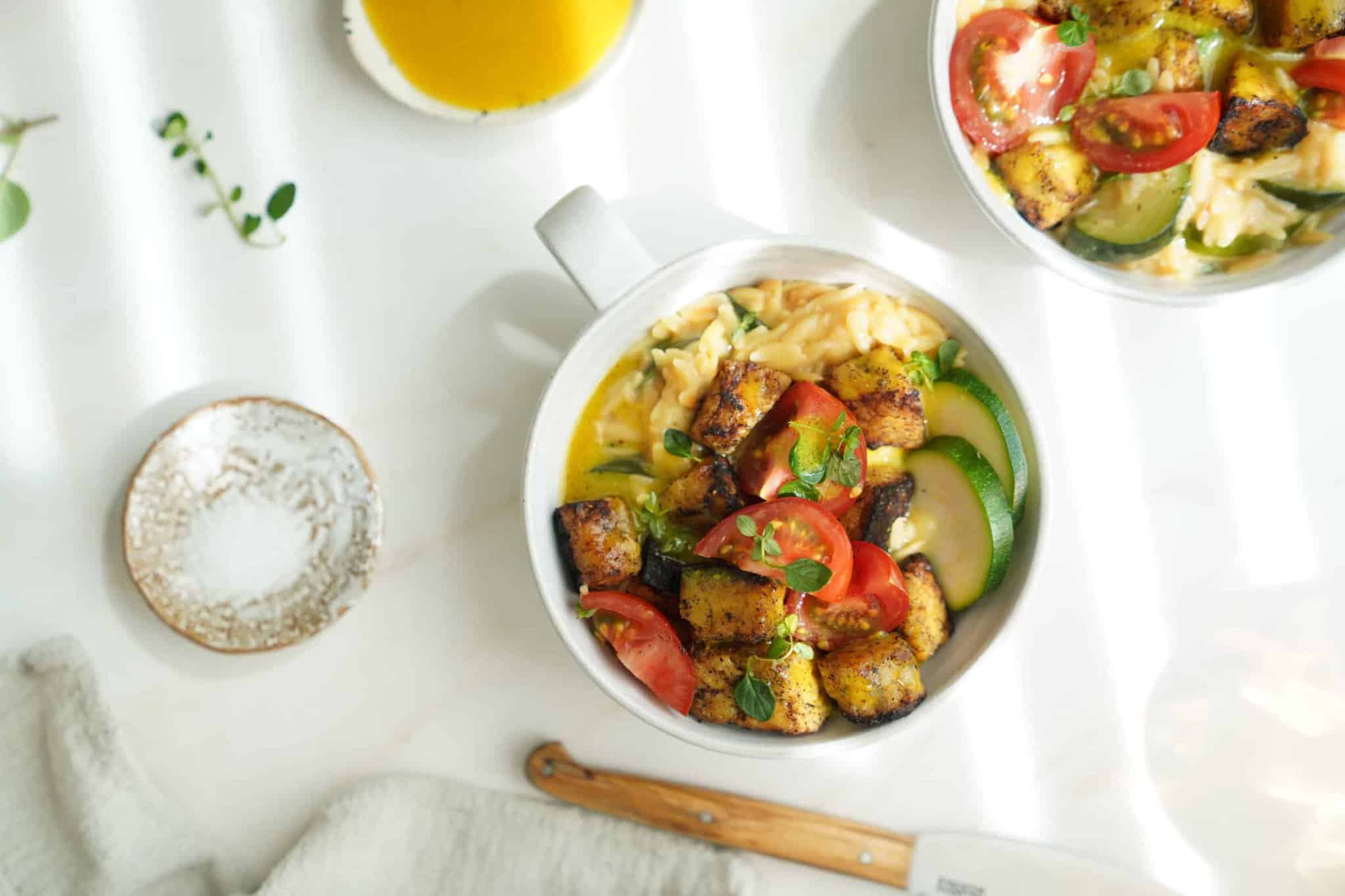 Greek tempeh with creamy orzo in a white bowl on a white counter