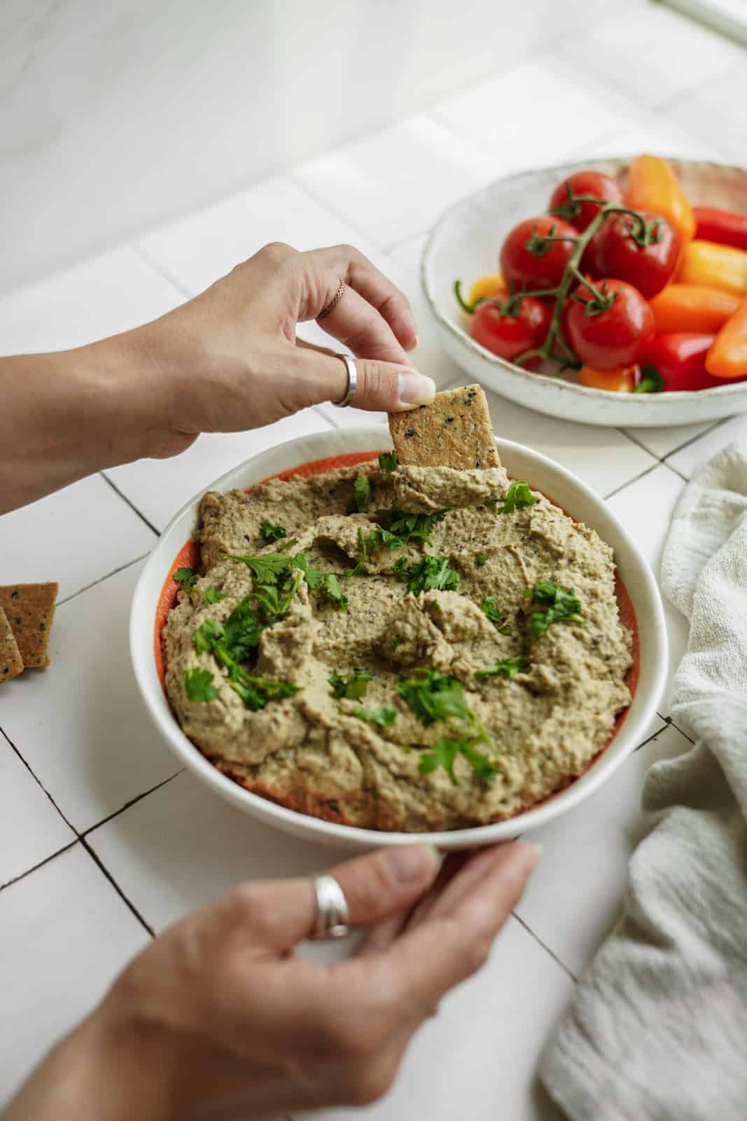 Big bowl of creamy eggplant dip with hand dipping cracker into it