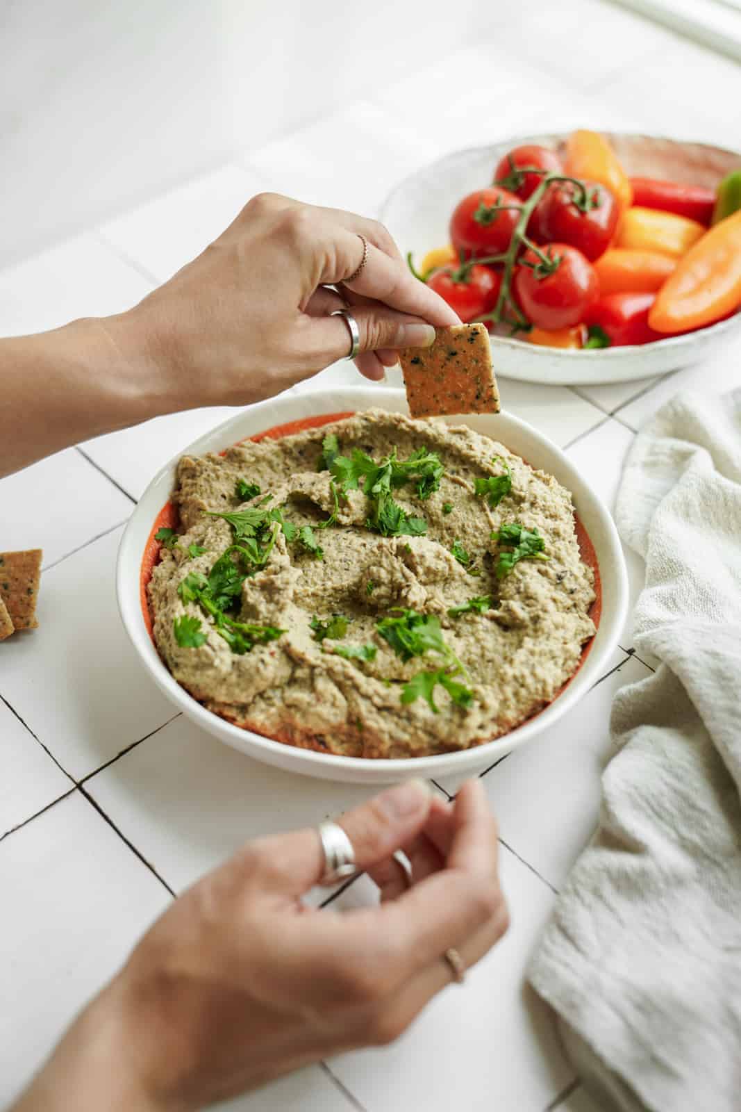 Large bowl of eggplant dip with cracker dipping into it